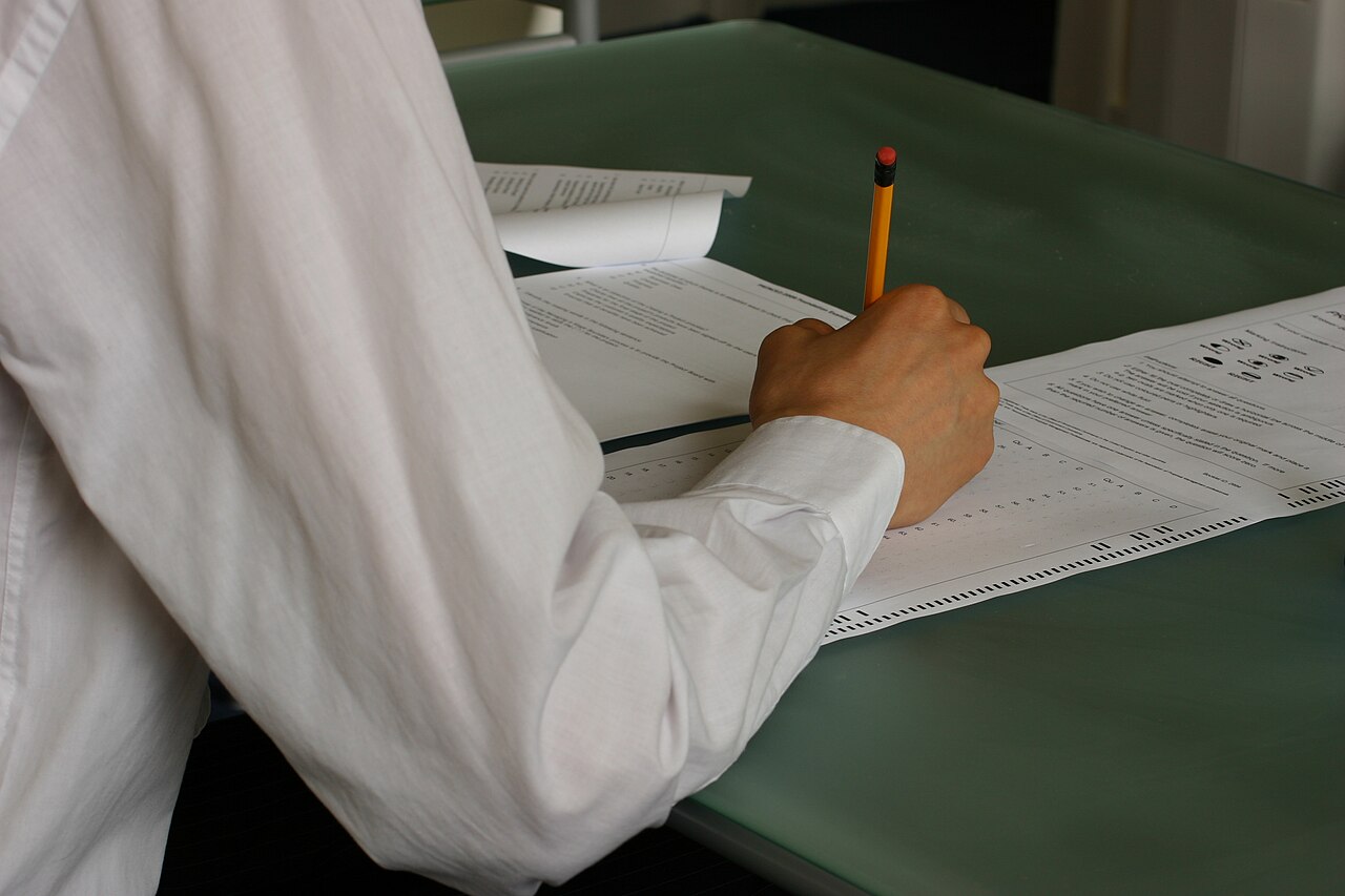 A student writes by hand in an exam classroom
