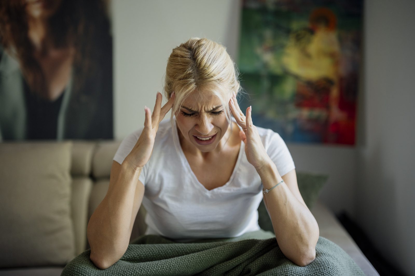 A woman holding her head in pain while sitting on a couch