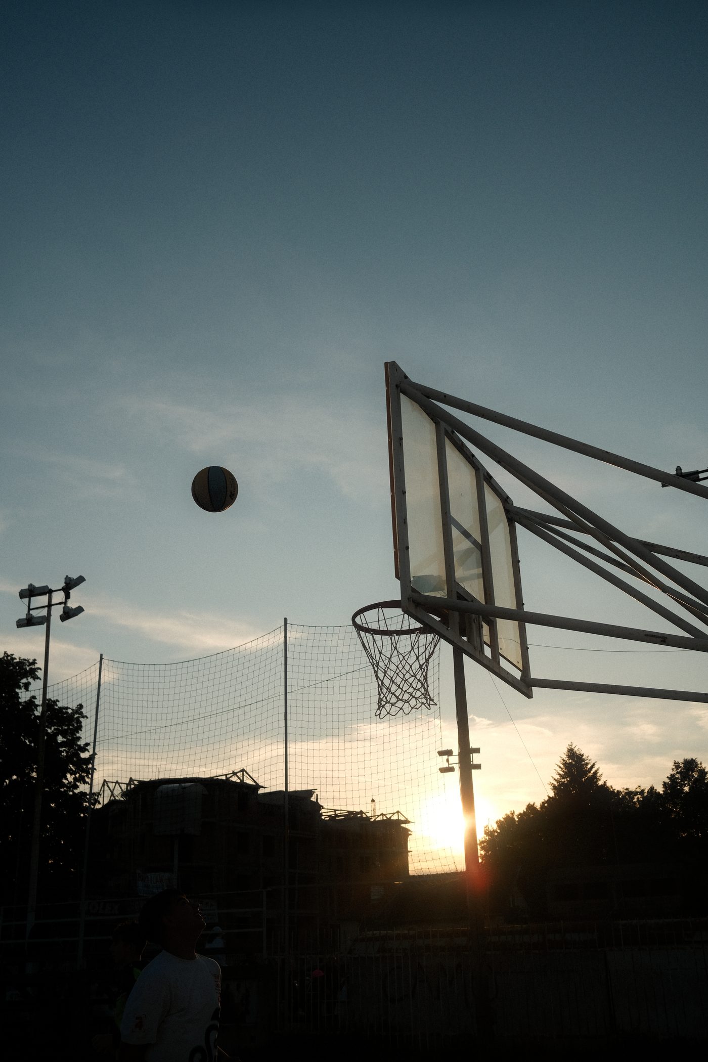 A basketball heads toward the hoop as the sun sets in the background