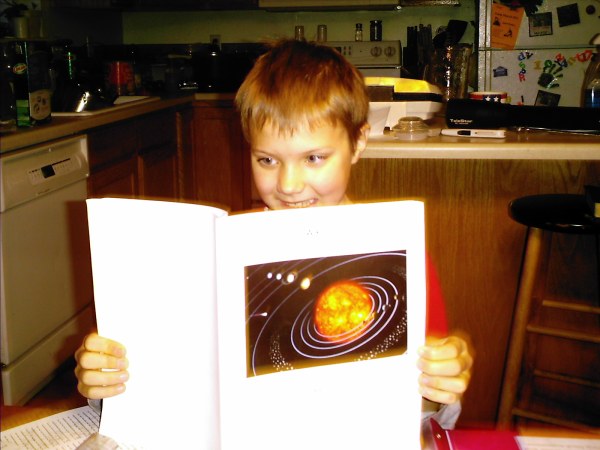 A boy reading a book about the solar system at a table
