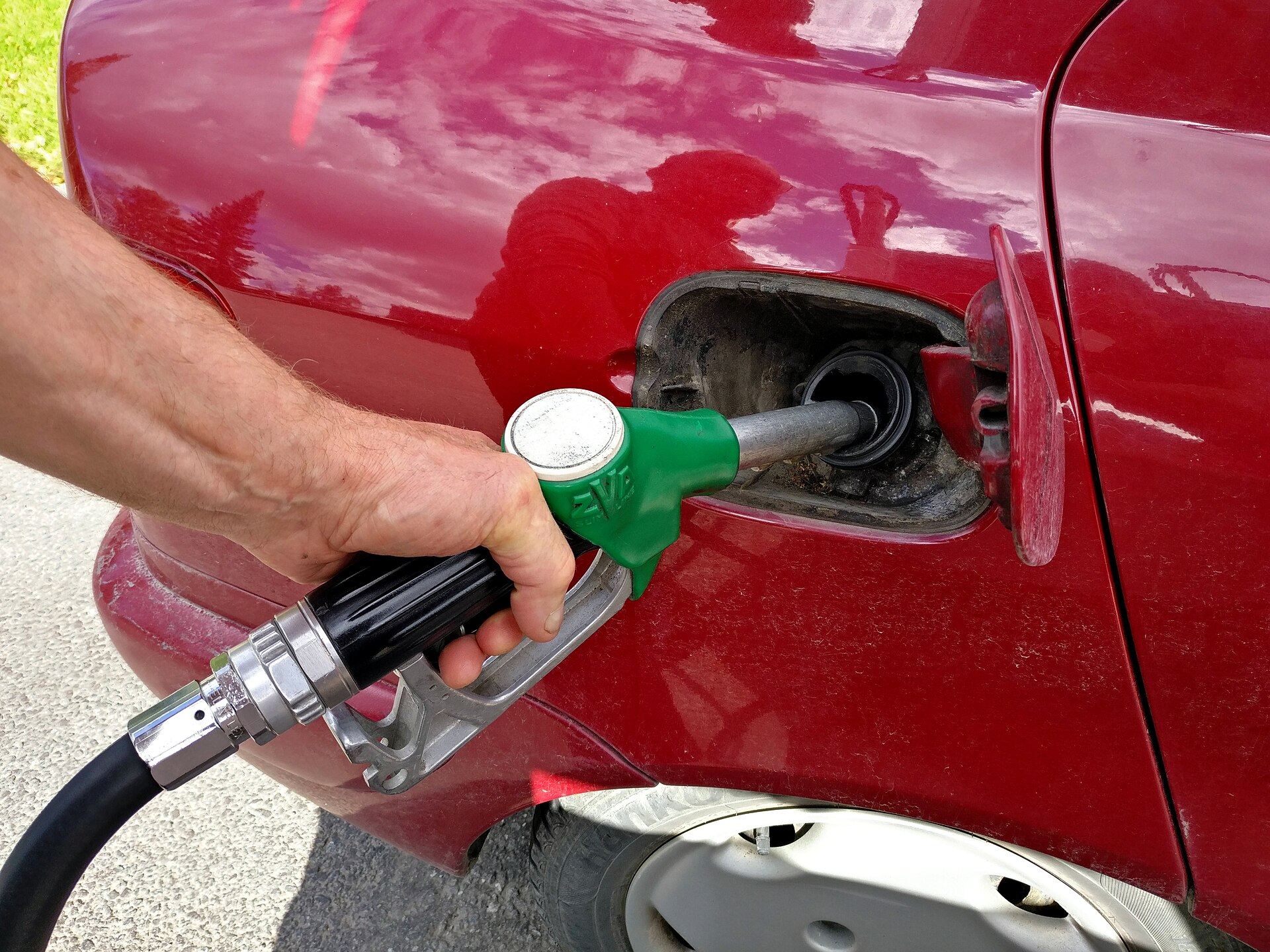 Hand holding a fuel nozzle while refuelling a red car