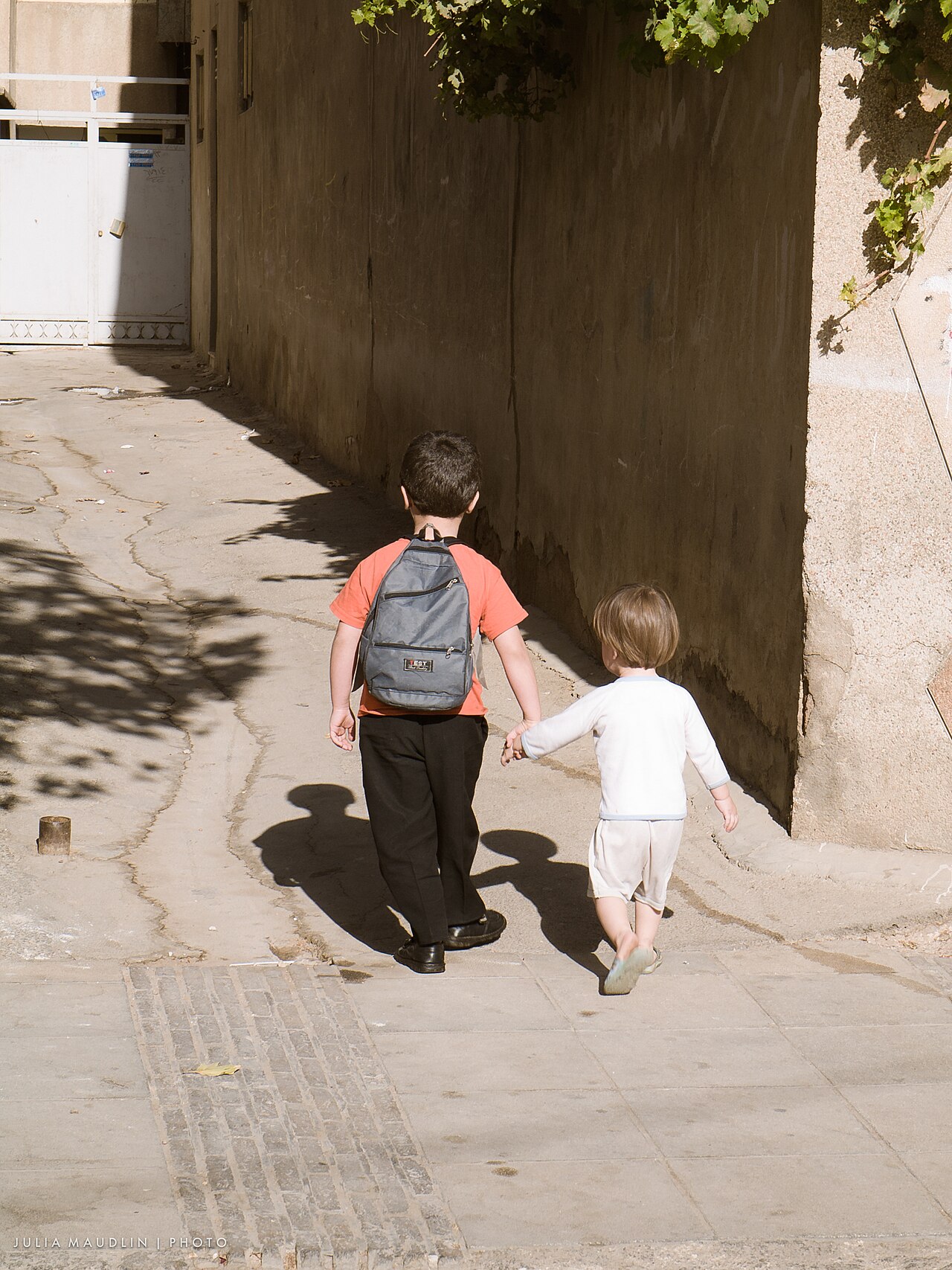 An older brother holding his younger brother's hand on the way home from school