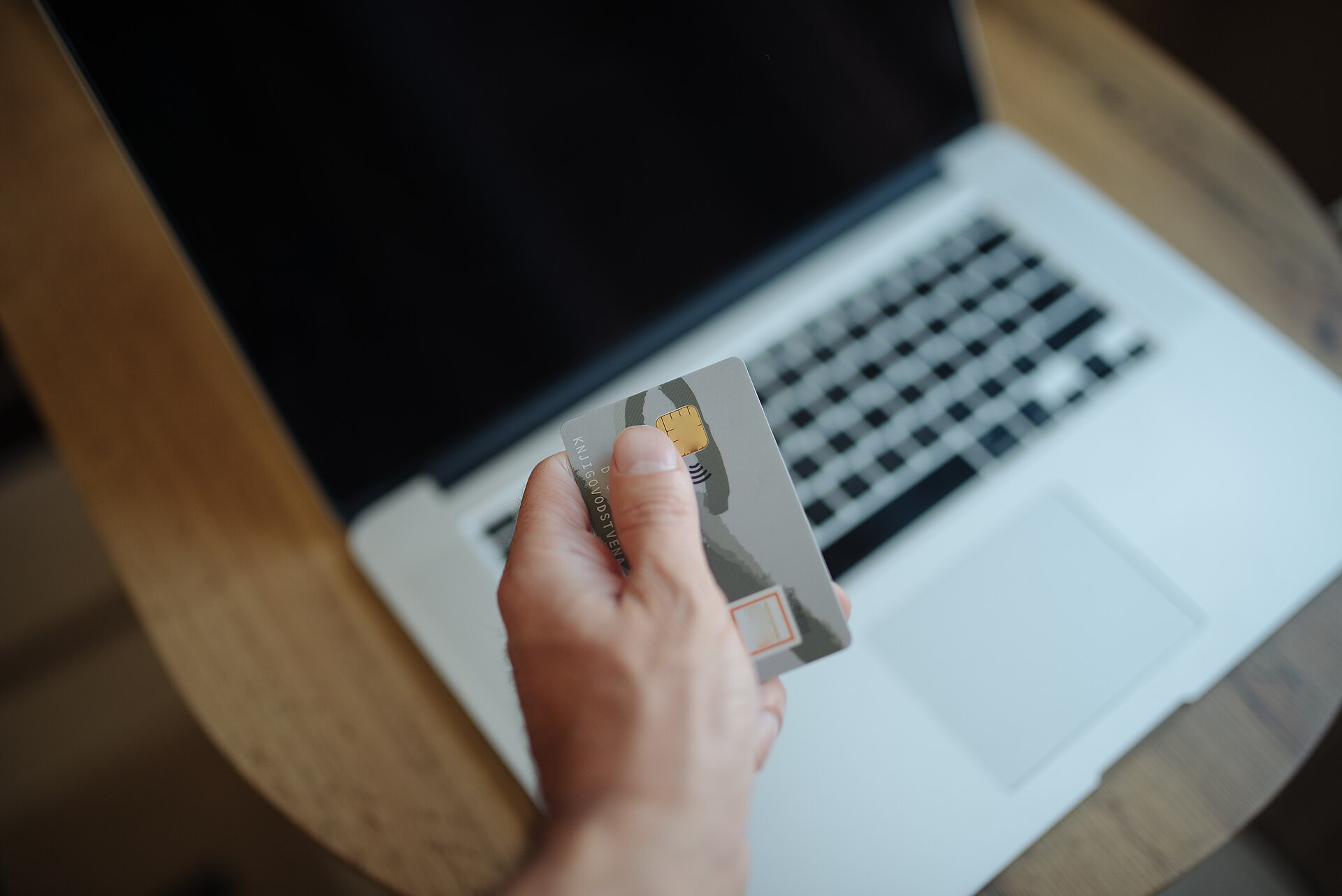 A hand holds a payment card over a laptop keyboard