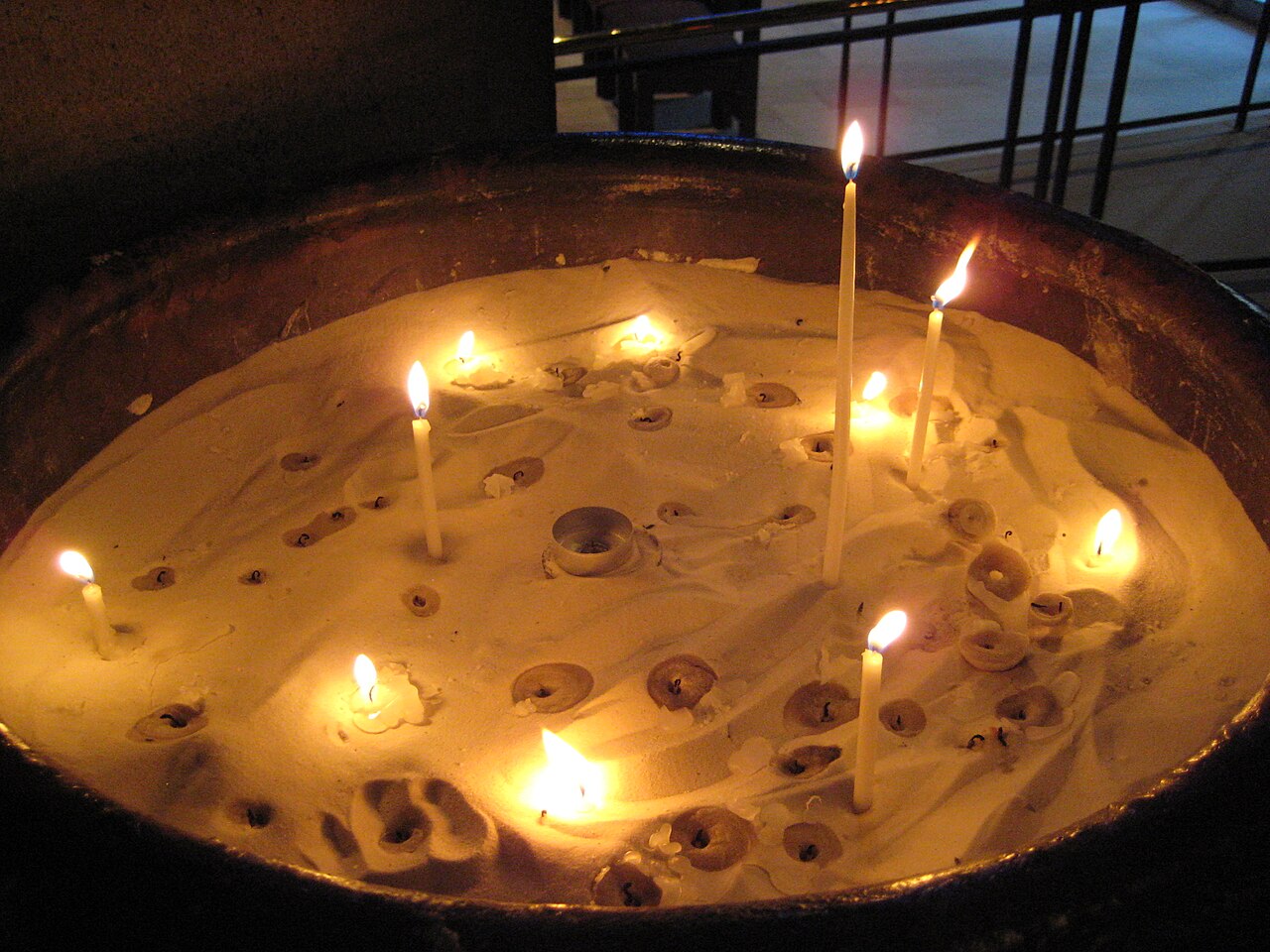 Candles burning in a basin of melted wax, showing how wax liquefies and spreads