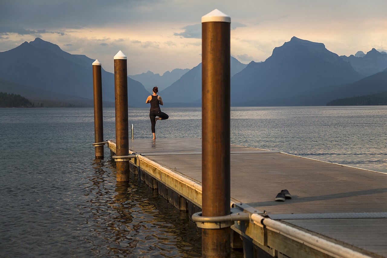 A person practicing tree pose outdoors by a lake