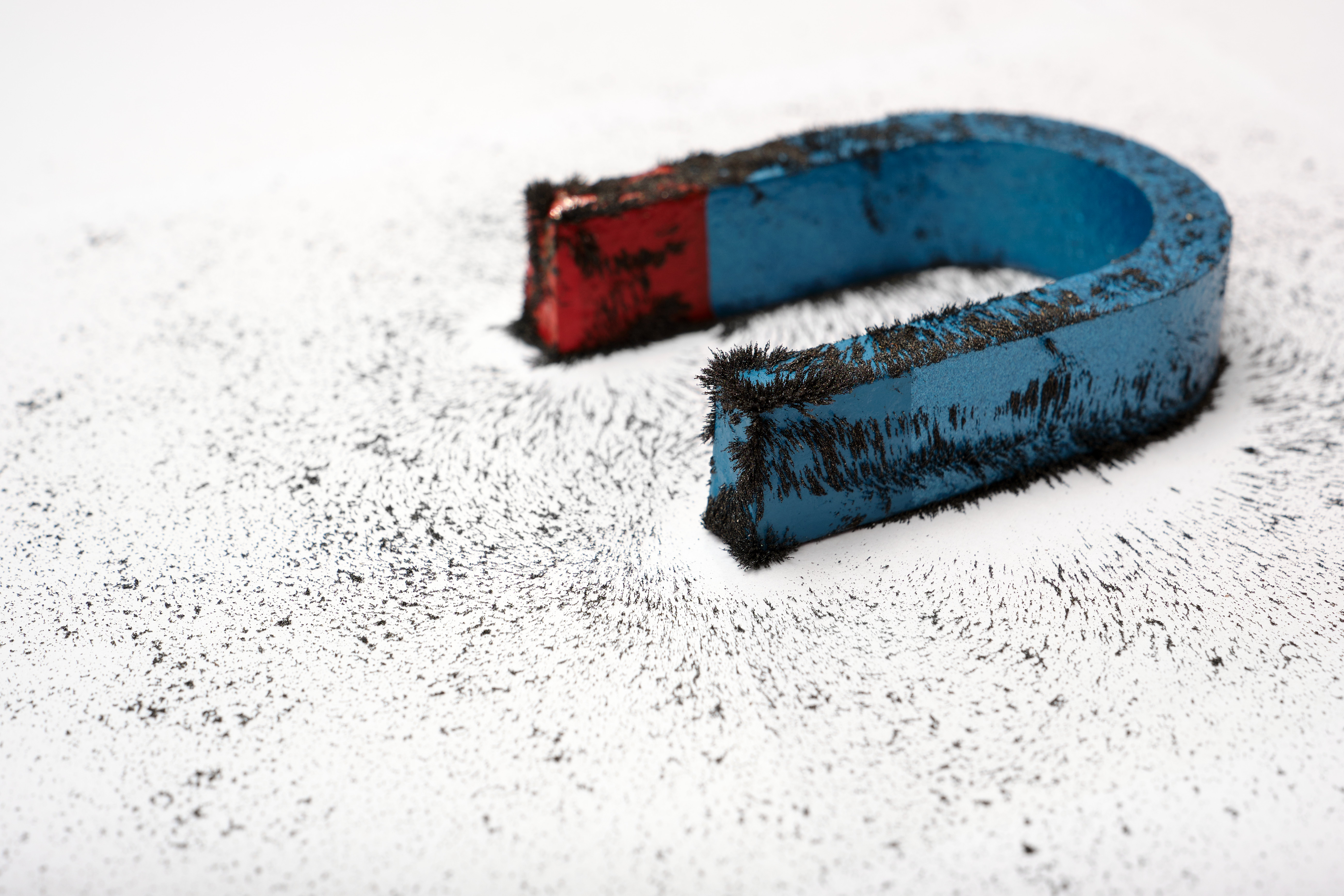A red horseshoe magnet covered in attracted metal shavings