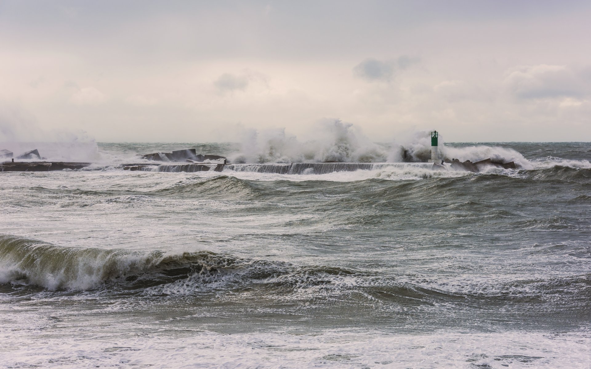 Ocean waves breaking against a pier with white foam under a gray sky
