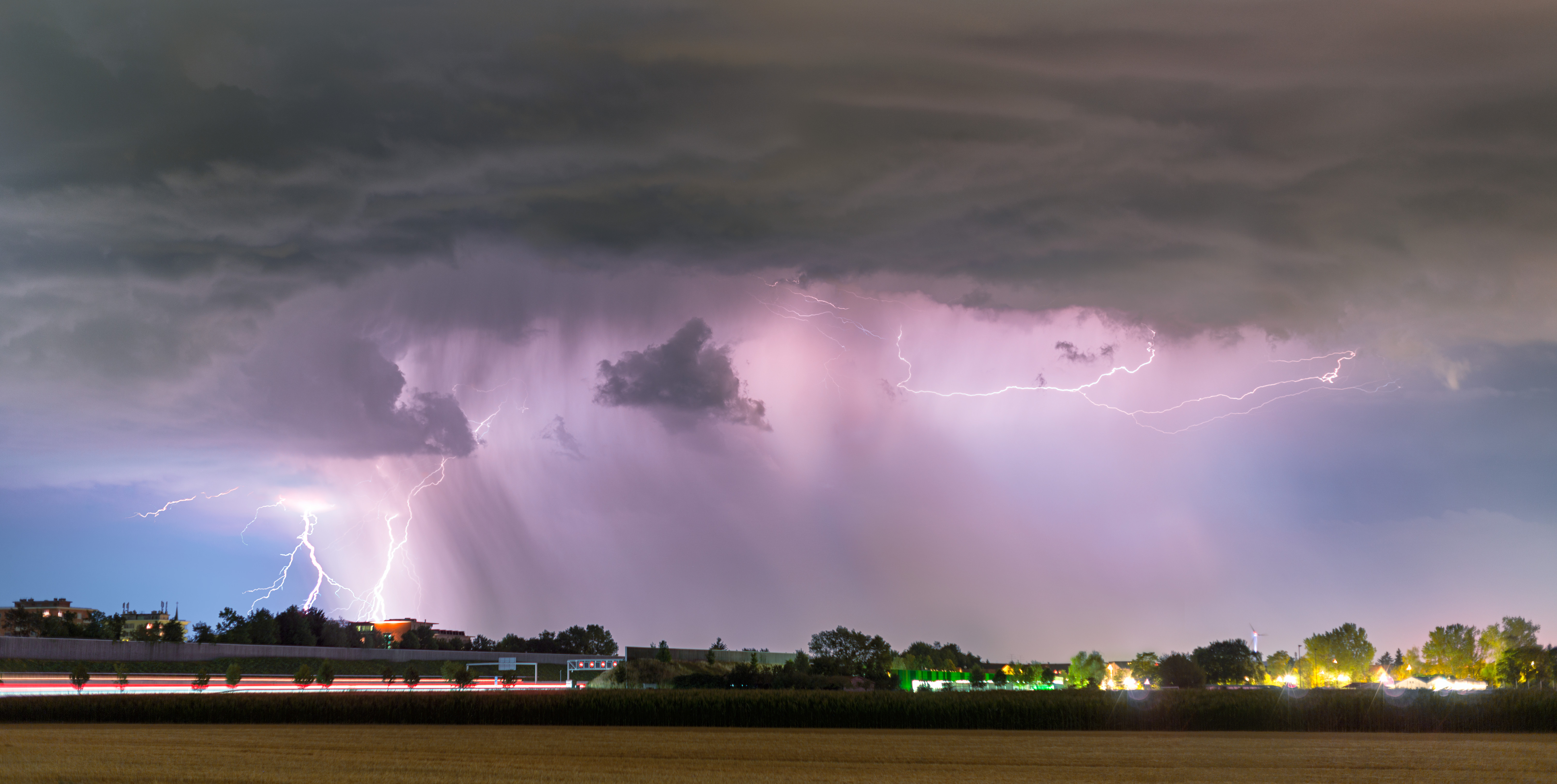 Lightning bolts striking through dark storm clouds over a field at night