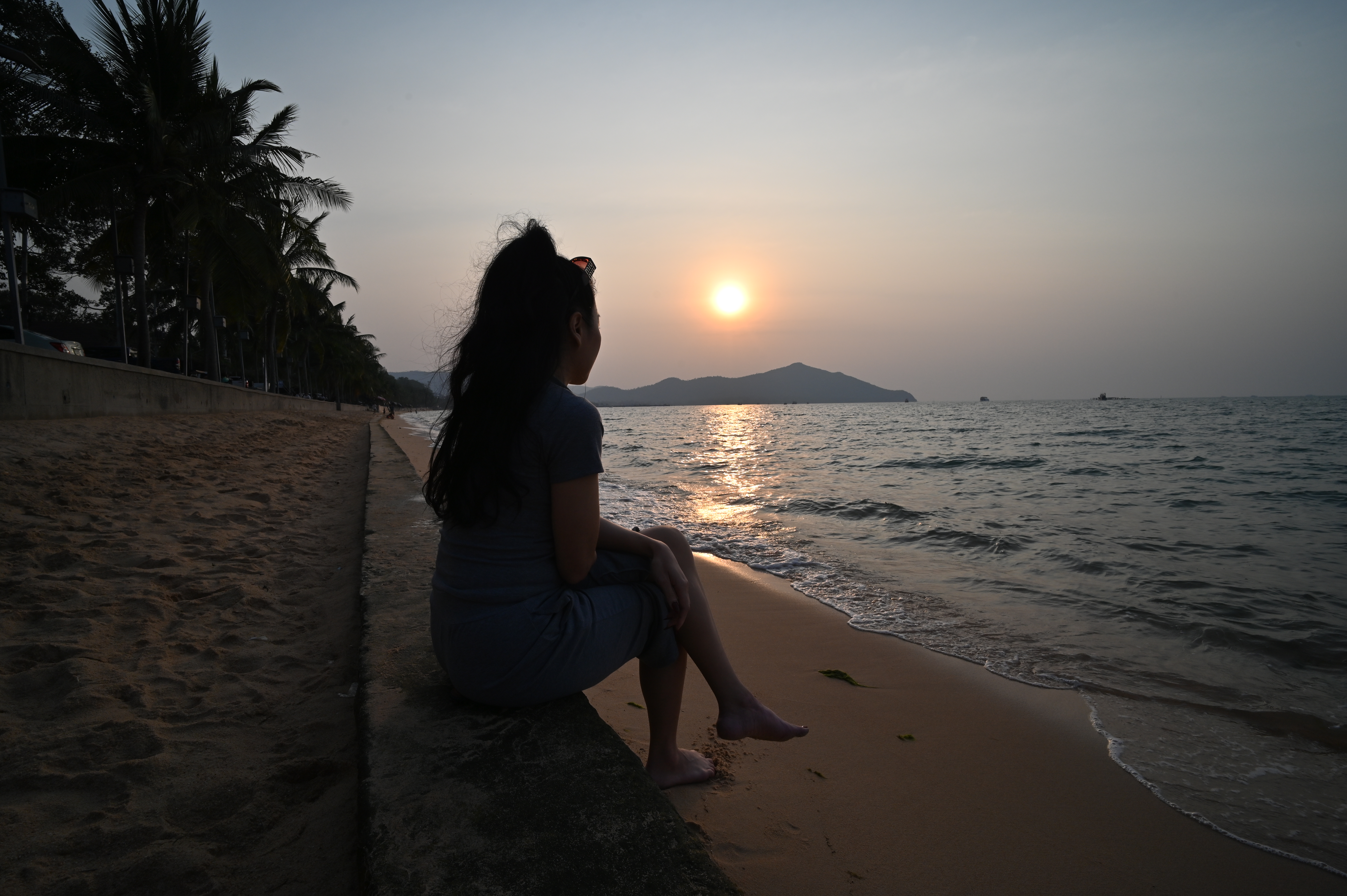 A person sitting on a beach watching an orange sunset over the sea
