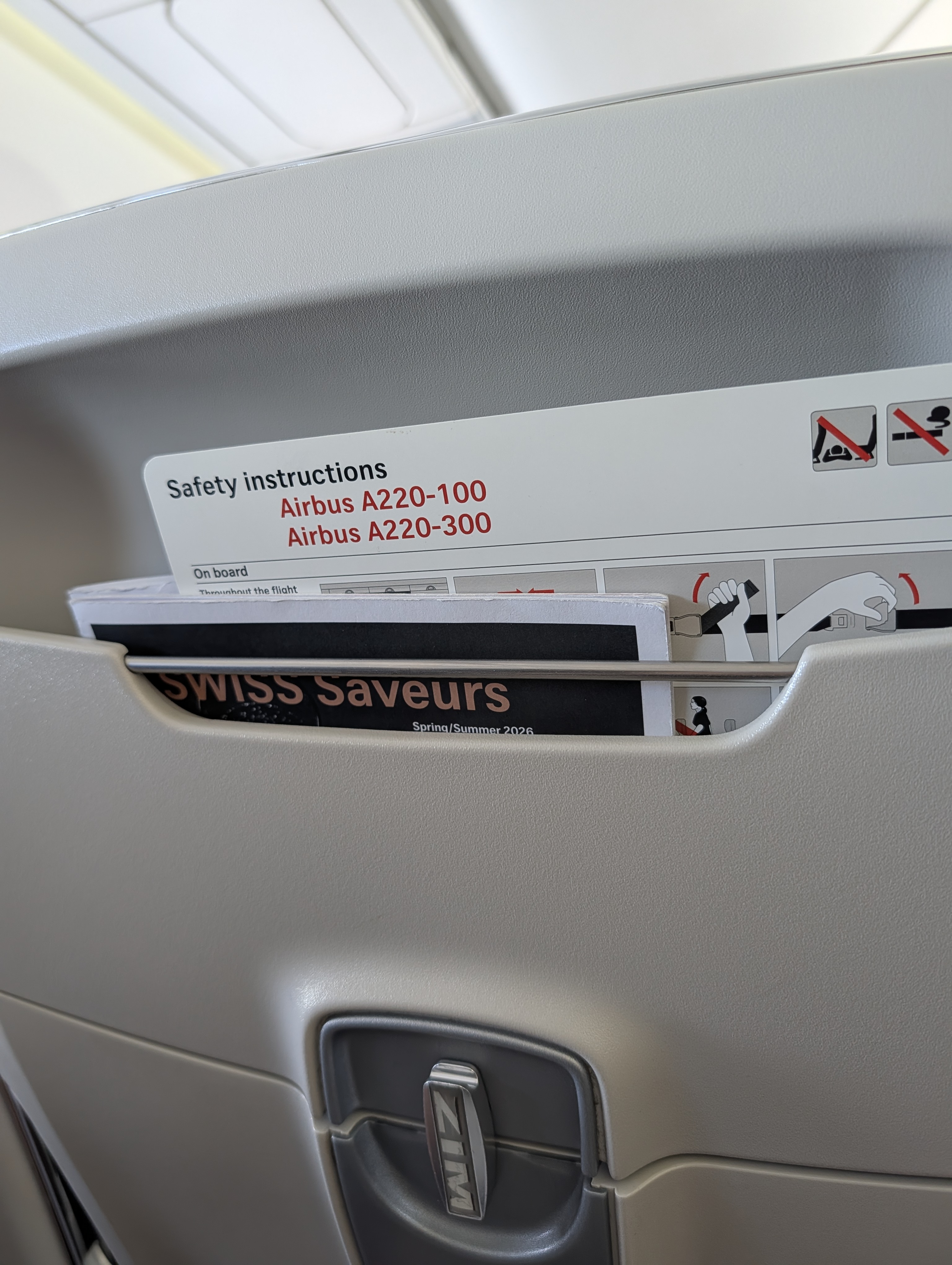 Close-up of an economy-class seatback with a safety instructions card in the seat pocket