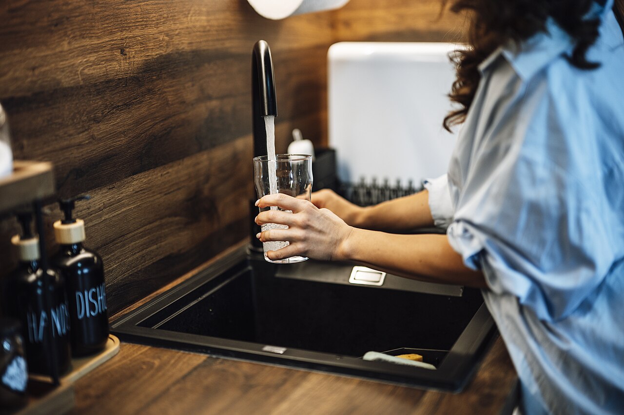 A person filling a glass with water from a kitchen tap