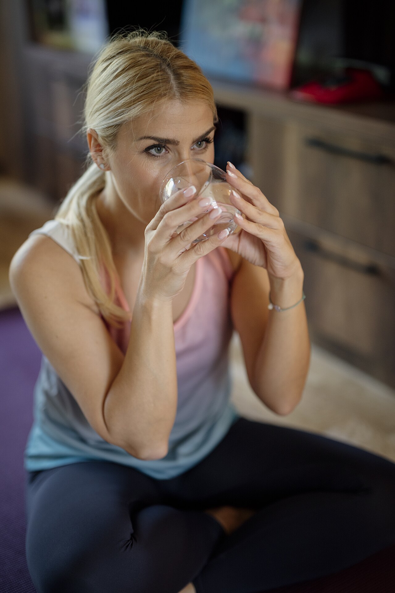 A woman drinking a glass of water, noticing its taste immediately
