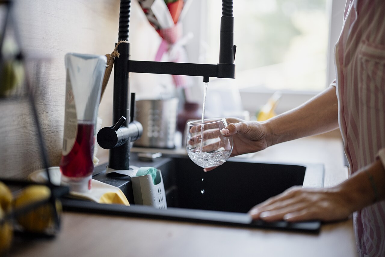Hands holding a glass under a running kitchen faucet