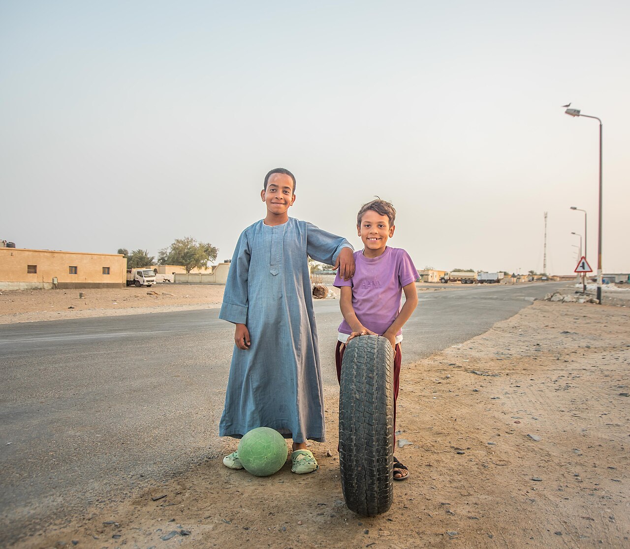 Two children playing together outdoors with a ball and a tire