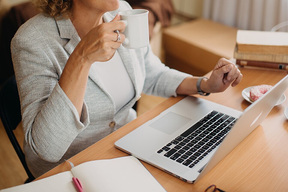 A woman in a blazer working at a home laptop with coffee, dressed fully for a video interview from home